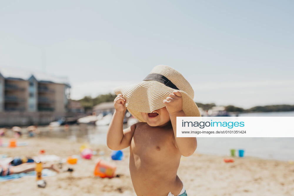 IMAGO Creative, Jahreszeit Sommer, Sonnenschutz Toddler Boy Playing Peek-a-boo with Sun Hat on Beach Milwaukee, WI, United States CR_SUWE200424C-371586-01,model released, Symbolfoto
