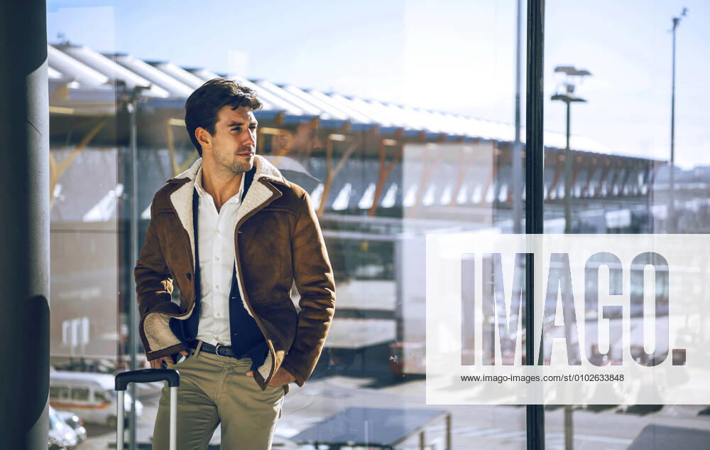Thoughtful businessman standing with hands in pockets by window at airport departure area model released Symbolfoto EHF00451