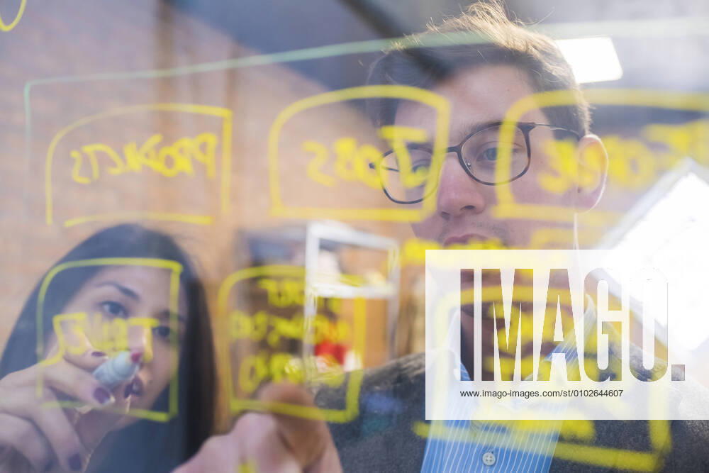 Businessman and woman brainstorming taking notes on glass pane in office model released Symbolfoto property released MEUF00850