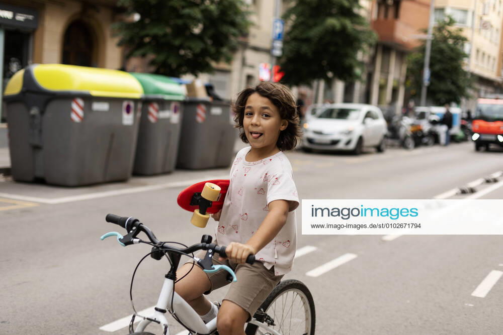 Carefree boy holding skateboard while riding bicycle on street model released Symbolfoto VABF03074