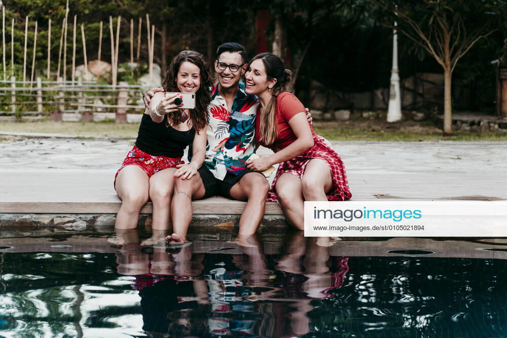 Smiling friends taking selfie while sitting at pool side model released Symbolfoto property released EBBF00732