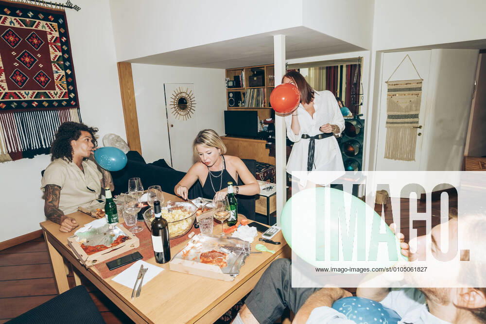 Male and female friends blowing balloons during party at home model released Symbolfoto property released MEUF01994