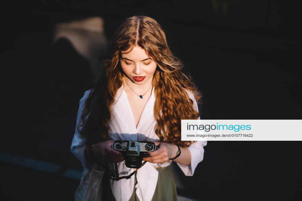 IMAGO Creative, Sommer, Schatten-Plätze bei Hitze Young woman holding analog film camera while standing in city CR_DMBE201207-477666-01 ,model released, Symbolfoto