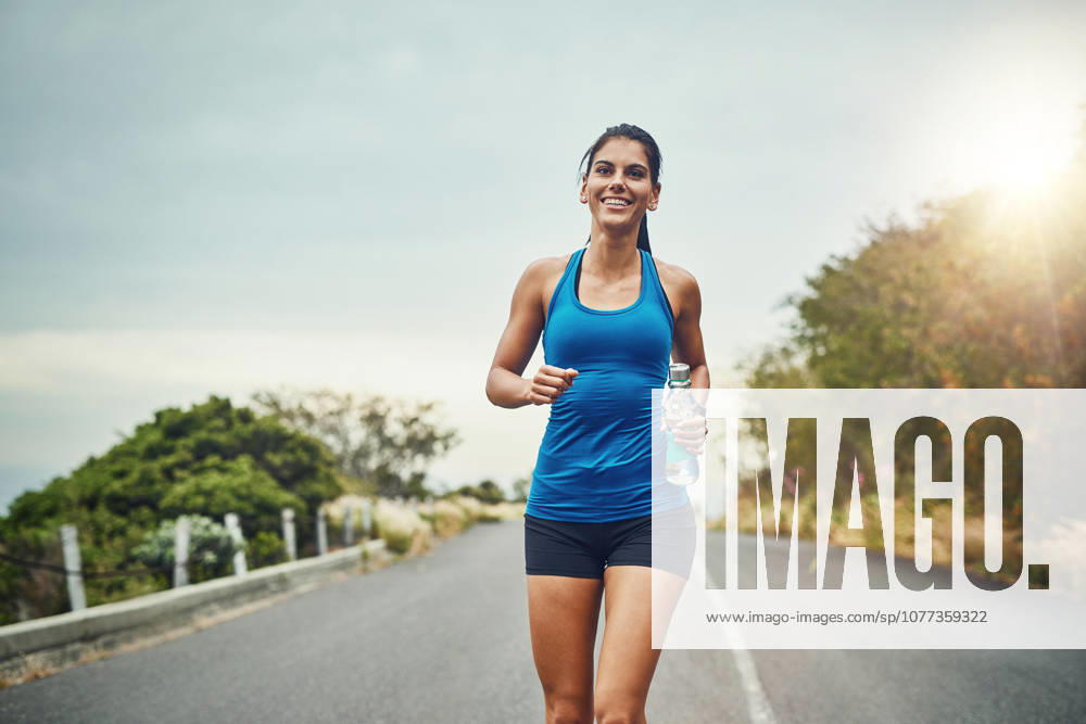 Fitness, happy woman and running with water bottle for exercise, cardio or wellness on road in nature. Female athlete, smile or workout on trail for health, or marathon training with sportswear. (License=RF) 21834404 ,model released, Symbolfoto