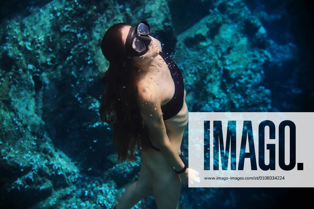 Young female diver in swimsuit and snorkeling mask floating in clean transparent sea water