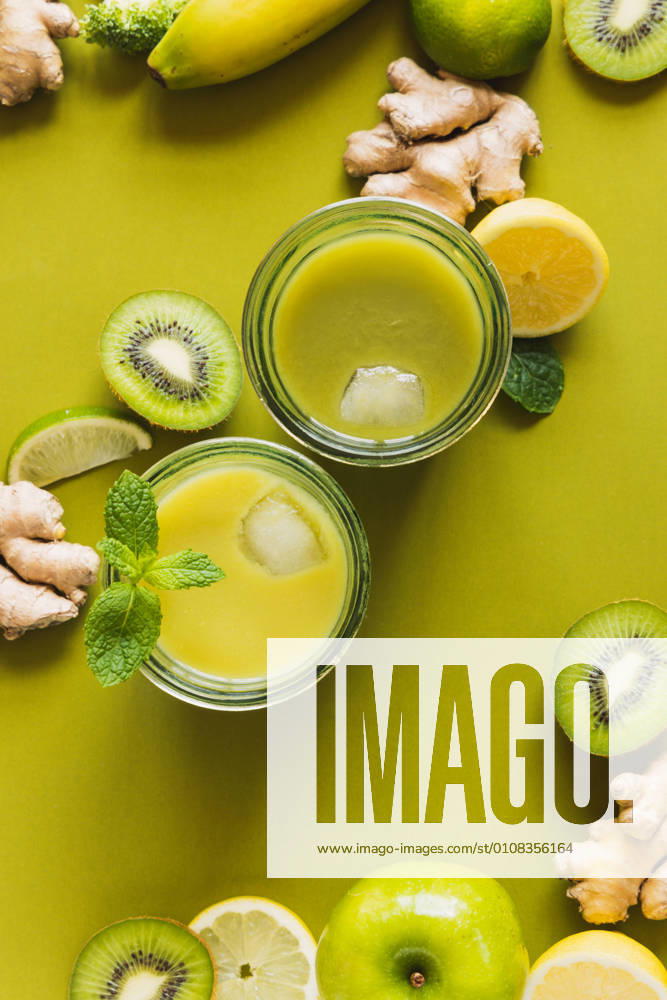 From above of glasses with healthy detox drinks with ice cubes placed on wooden tray with apple and ginger