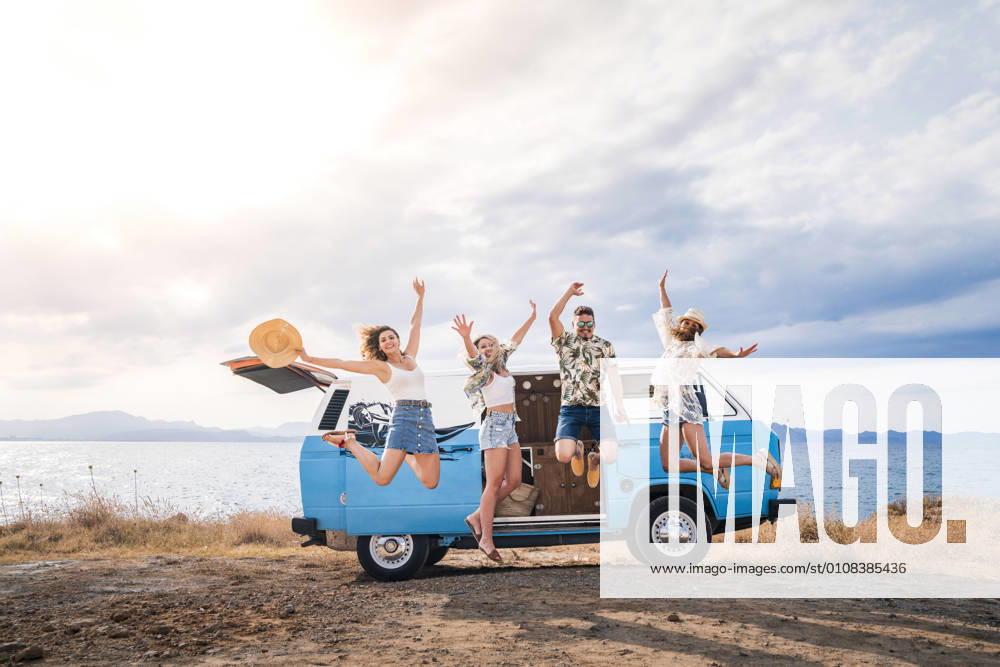 Cheerful tourist jumping raising hands and legs on background of bright minivan on beach in sunny day