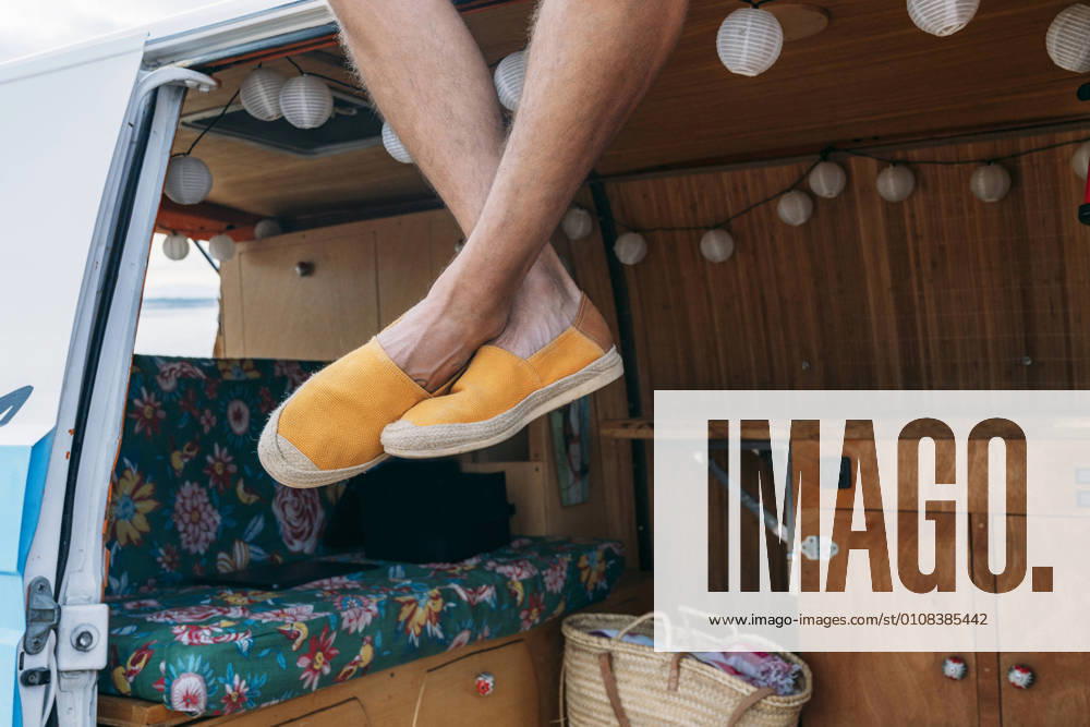 IMAGO Creative: Klimawandel - Nachhaltiges Reisen Legs of crop person in yellow fabric shoes hanging from car roof in bright day