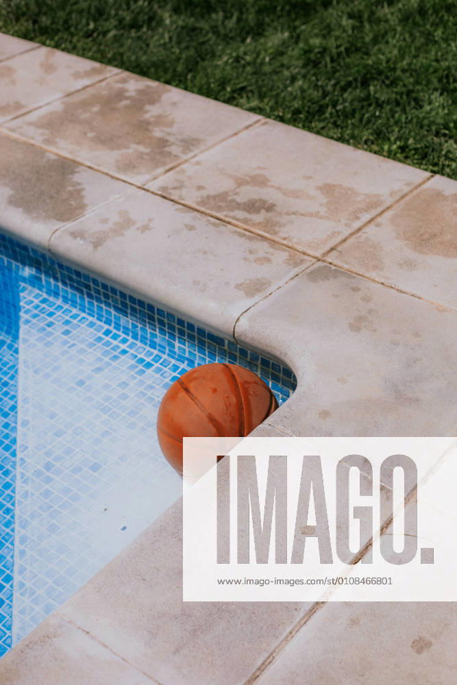 From above of basketball ball in corner on swimming pool in terrace of house with green grass