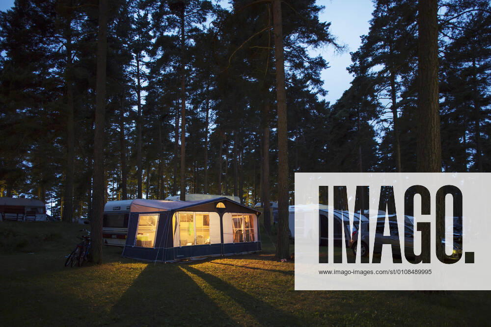 IMAGO Creative: Klimawandel - Nachhaltiges Reisen Caravans parked in travel trailer park by illuminated tent amidst trees at dusk
