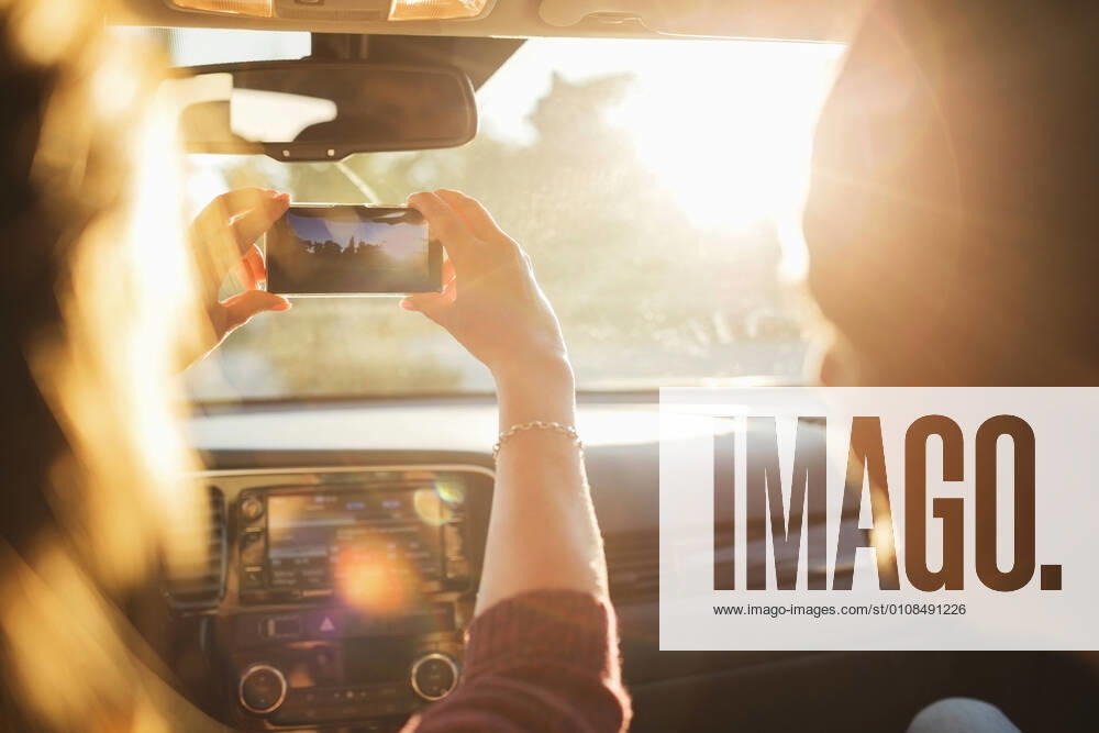 IMAGO Creative: Klimawandel - Nachhaltiges Reisen Man looking at woman photographing from mobile phone through car windshield , model released