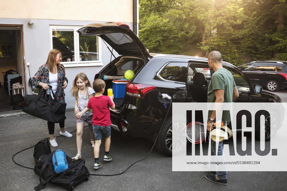 IMAGO Creative, Jahreszeit Sommer, Sommerferien Family with luggage and black electric car in back yard , model released, property released