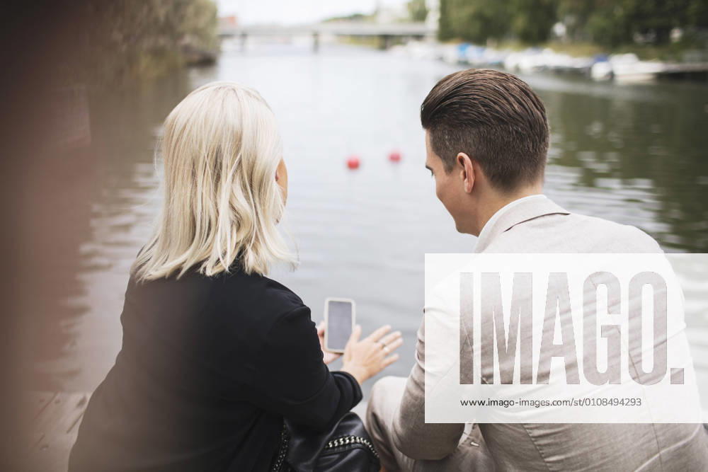 IMAGO Creative, Jahreszeit Sommer, Sommer in der Stadt Rear view of business people discussing mobile phone against lake , model released, property released
