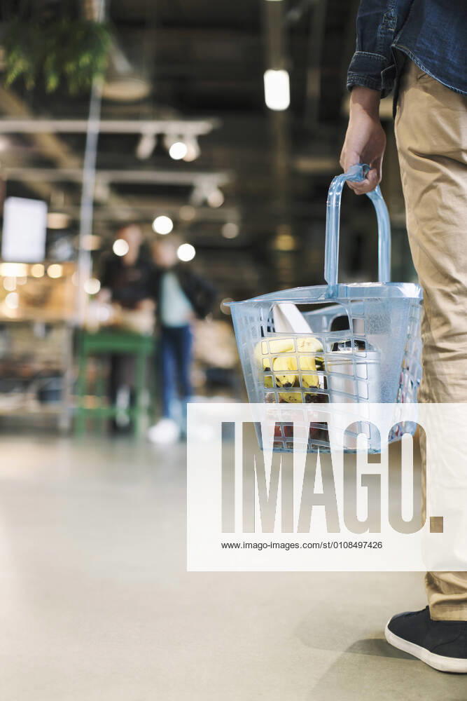 IMAGO Creative: Landleben - Essen Low section of man carrying grocery basket in supermarket , model released, property released