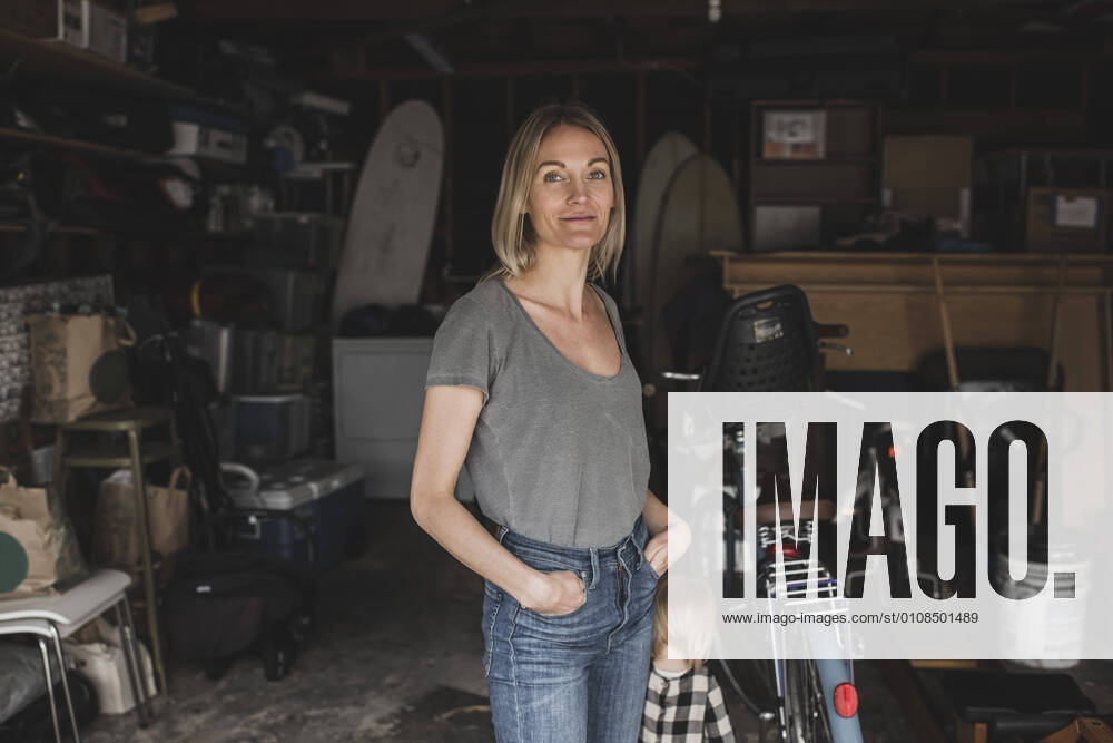 Portrait of mid adult woman standing with hands in pockets by daughter at storage room , model released, property released