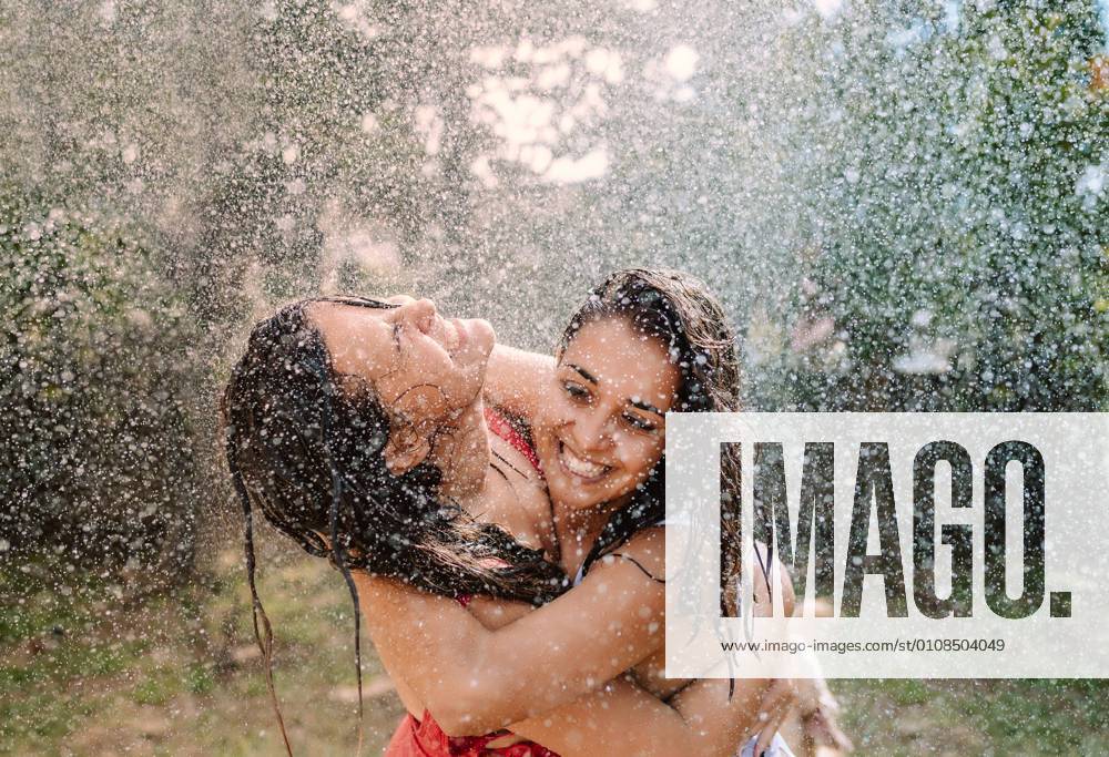 Friends in swimsuits hugging under water drops, Model released