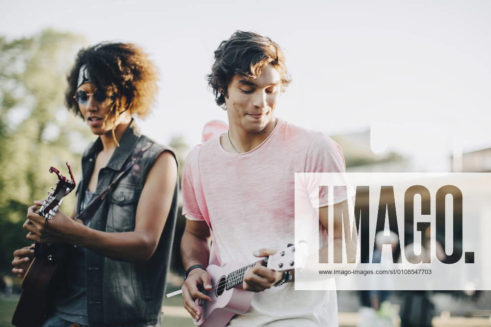 Happy young men playing ukulele at music concert in summer , model released