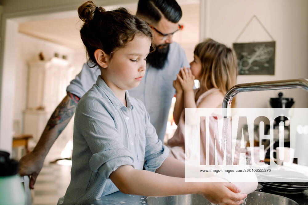 Girl washing mug at sink while father talking to daughter in kitchen , model released, property released