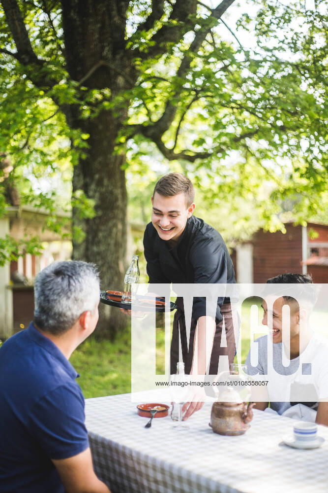 IMAGO Creative: Landleben - Essen Smiling young waiter talking with customers while working at outdoor cafe , model released, property released
