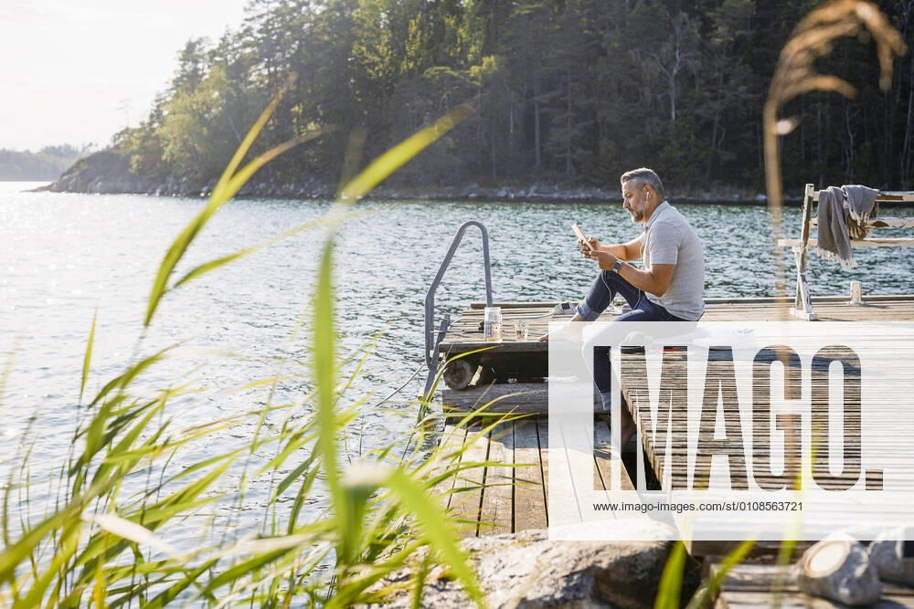 Full length of man using digital tablet while sitting on wooden pier over lake at forest , model released, property released