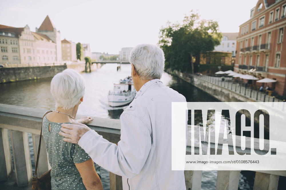IMAGO Creative, Jahreszeit Sommer, Sommer in der Stadt Rear view of senior couple standing on bridge against railing in city , model released