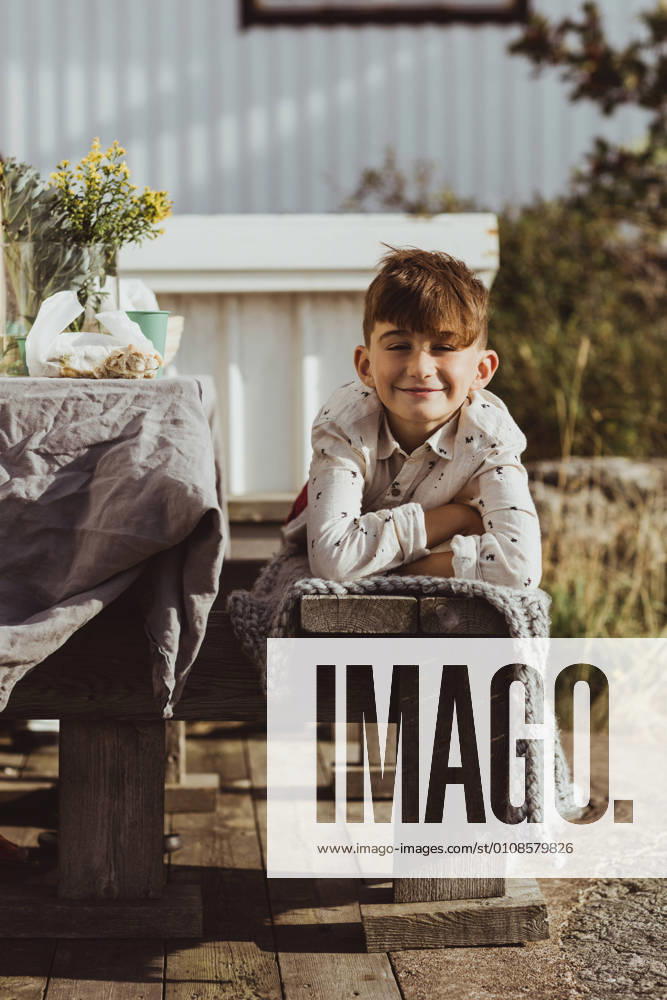 IMAGO Creative, Jahreszeit Sommer, Sommerferien Portrait of smiling boy lying on front over wooden seat Sweden, Gothenburg, model released, property released