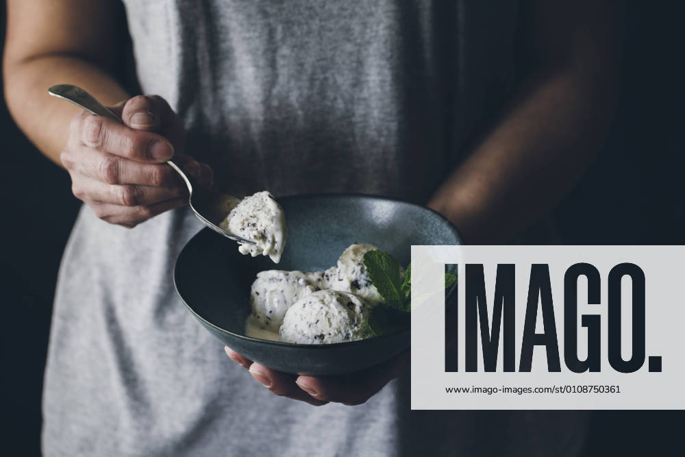 Crop view of anonymous woman with spoon in hand and holding bowl with stracciatella ice cream balls decorated with mint leaves