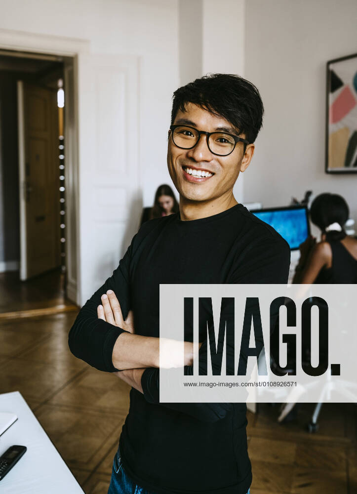 Happy businessman with arms crossed standing in office Germany, Berlin, model released, property released