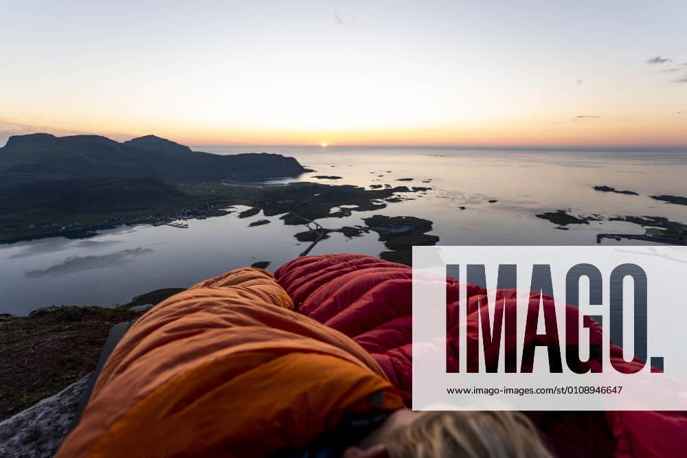 Hiker lying in sleeping bag against sea at Volandstinden, Lofoten, Norway model released Symbolfoto MALF00252