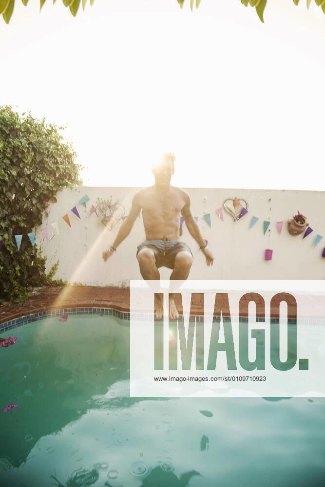 Shirtless man jumping into swimming pool against sky during sunset model released Symbolfoto property released AJOF00299