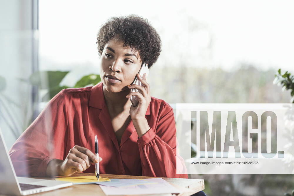 Woman talking on mobile phone and looking at laptop at desk model released Symbolfoto property released UUF22462