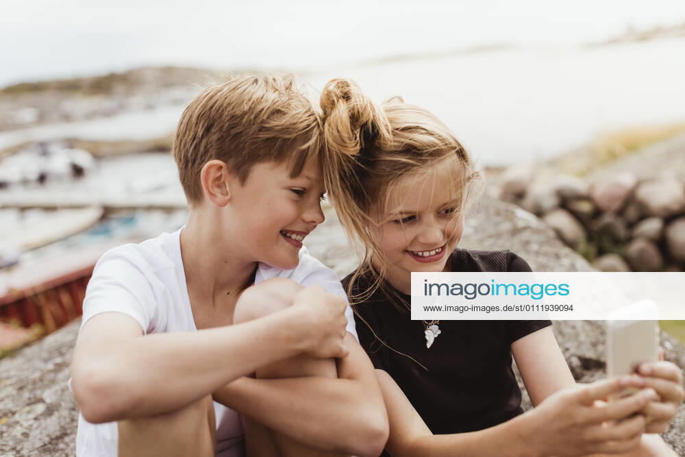 Smiling brother and sister taking selfie on smart phone at marina Sweden, Gothenburg, model released
