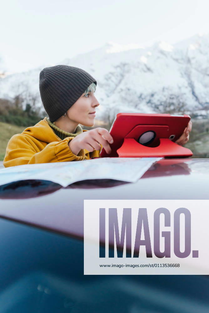 IMAGO Creative: Klimawandel - Nachhaltiges Reisen Content young female in warm clothes browsing tablet on car roof and looking away while standing on mountainous terrain on freezing winter day, Model released