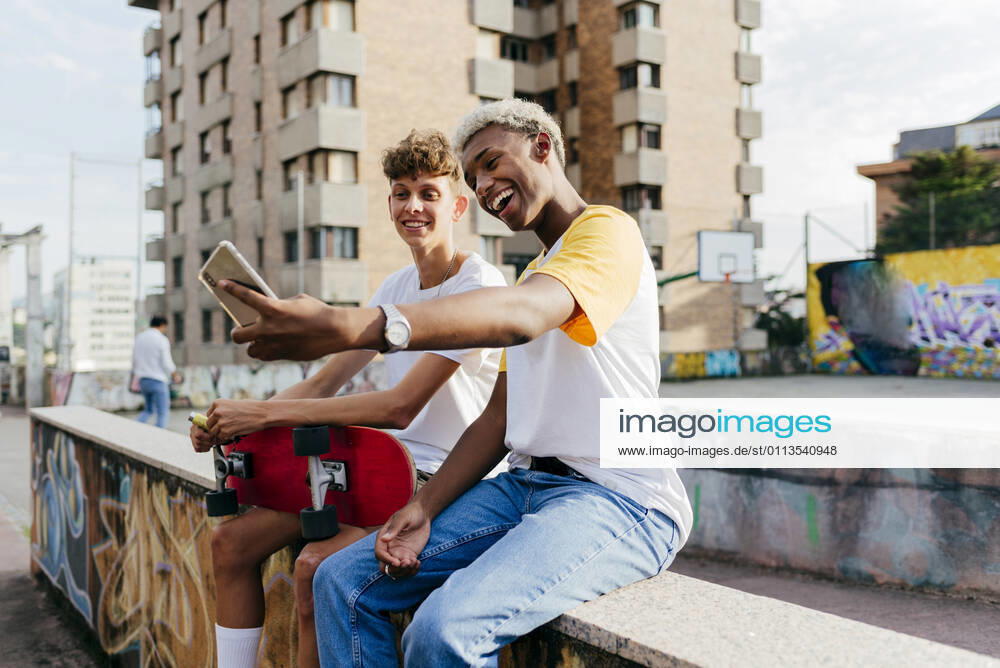 IMAGO Creative, Jahreszeit Sommer, Sommerferien Two handsome teenage boys with skateboard taking selfie on the street, Model released, Property released
