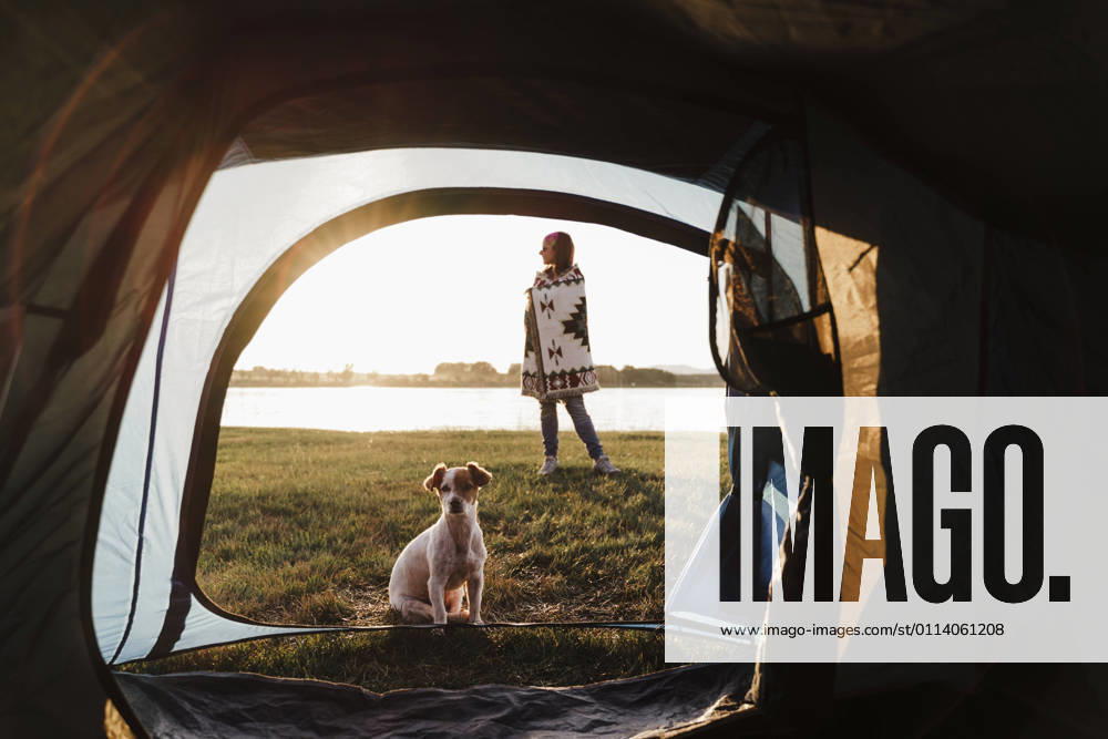 Woman wrapped in shawl camping with dog against lake seen through tent model released Symbolfoto property released EBBF02198