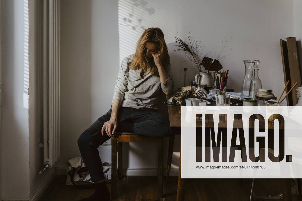 Depressed woman sitting on chair in living room Germany, Berlin, model released, property released