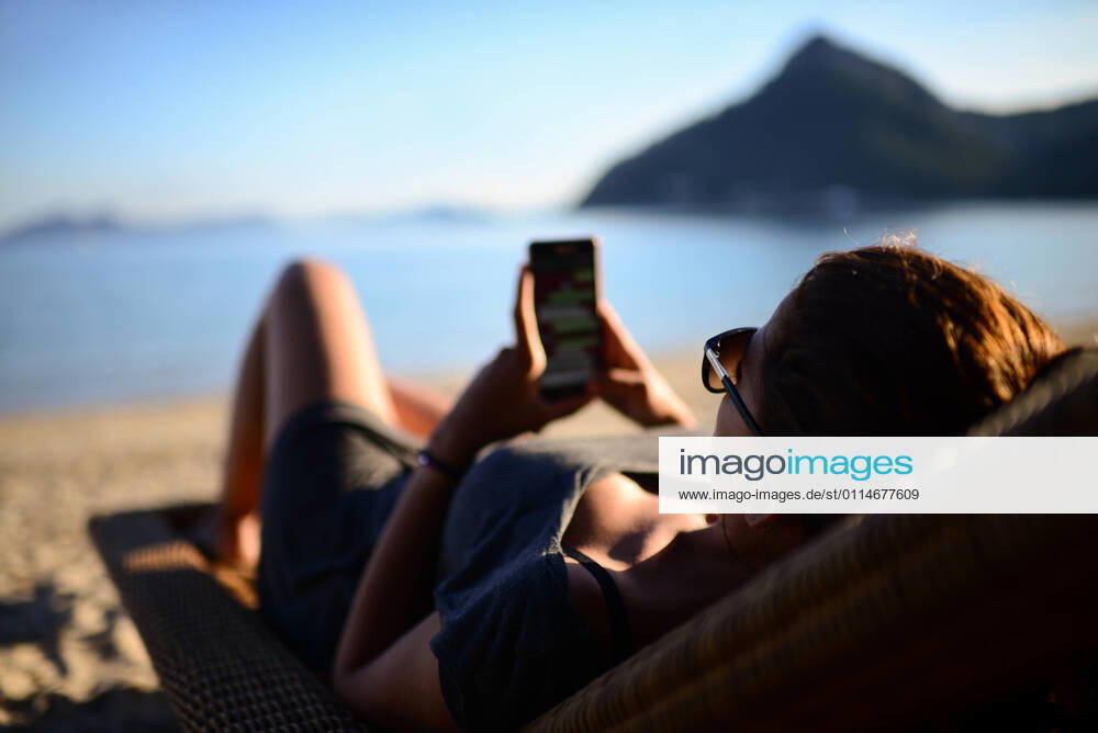 IMAGO Creative, Jahreszeit Sommer, Sommerferien Young woman uses the smartphone on the beach Palma, IB, Spain CR_RBIG210305-670348-01 ,model released, Symbolfoto
