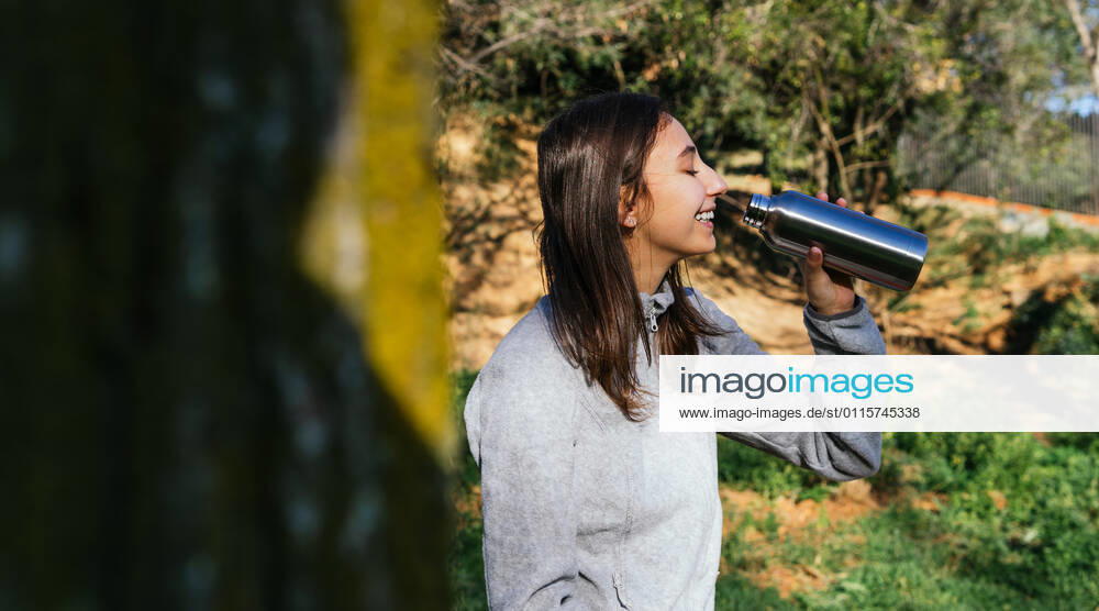 Side view of crop female hiker standing in forest and enjoying fresh water from metal bottle during hiking, Model released