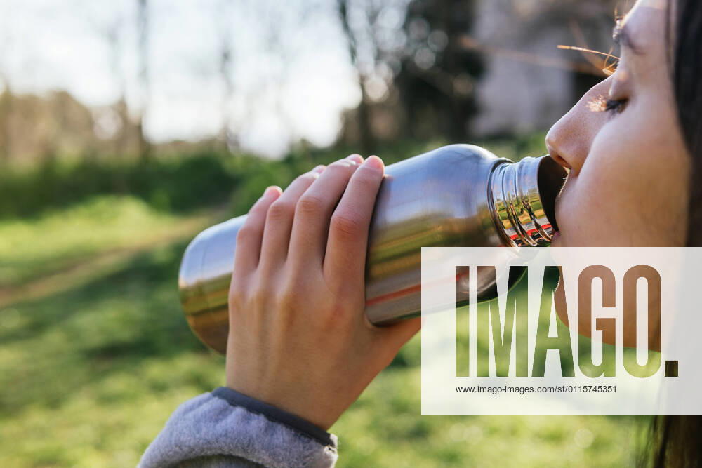 Side view of crop female hiker standing in forest and enjoying fresh water from metal bottle during hiking, Model released