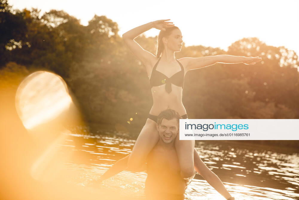 Young woman sitting on shoulders of young man standing in lake, enjoying the sun model released Symbolfoto GUSF02346