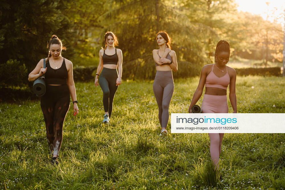 IMAGO Creative: Sommer, Abendspaziergang Confident fit multiracial female athletes walking with mat along lawn during training in summer park in evening, Model released