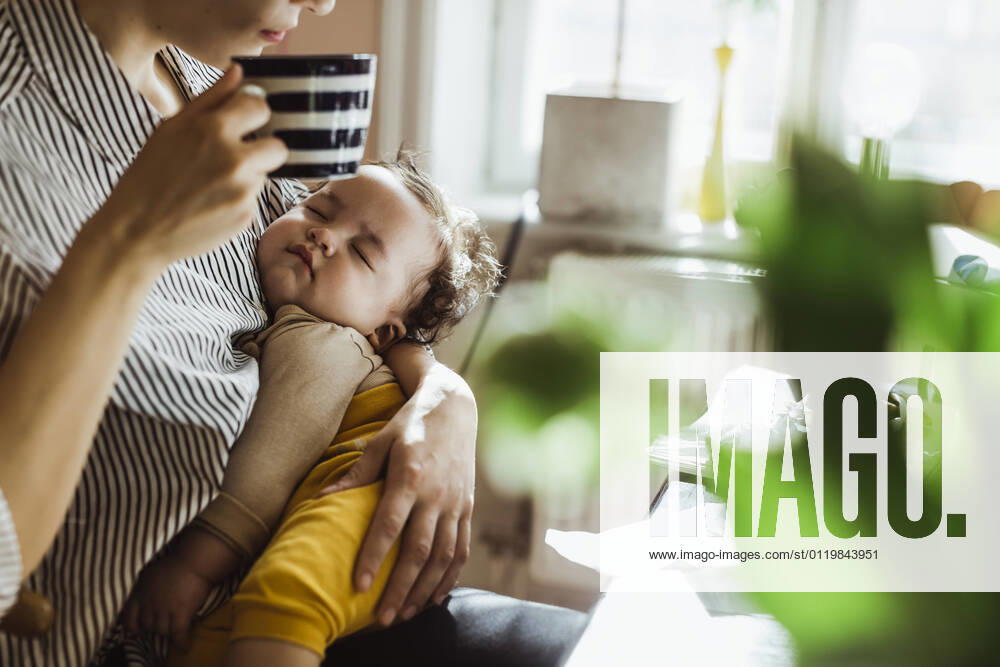 Midsection of mother drinking coffee while carrying sleeping baby boy at home Sweden, Stockholm, model released, property released