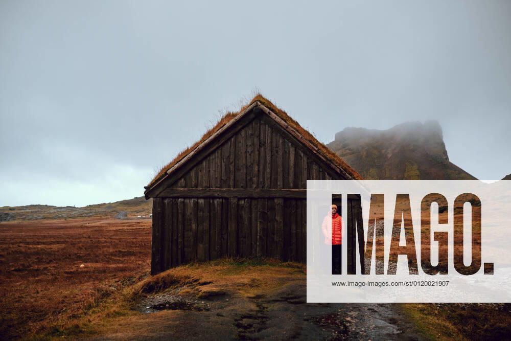 IMAGO Creative: Klimawandel - Nachhaltiges Reisen Young tourist standing near hut between wild lands near high stone hills and cloudy sky, Model released