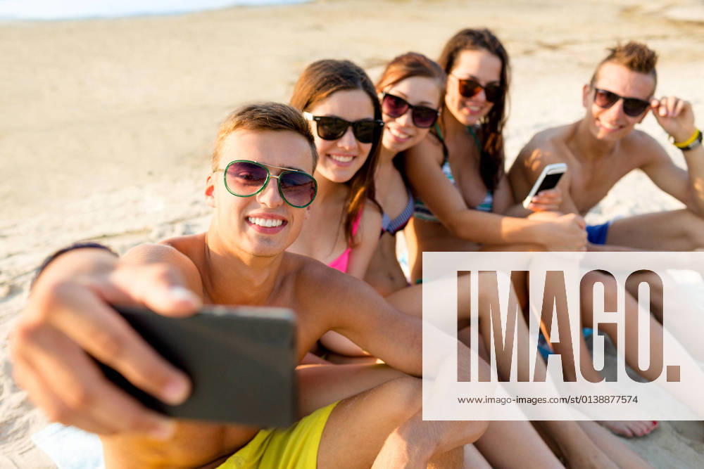 IMAGO Creative, Jahreszeit Sommer, Sommerferien friendship, leisure, summer, technology and people concept - friends sitting and taking selfie with smartphone on beach