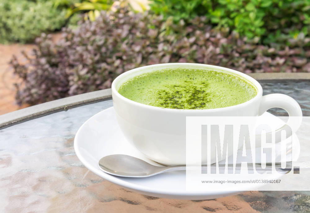 Closeup a cup of matcha latte or green tea on glass table with nature background