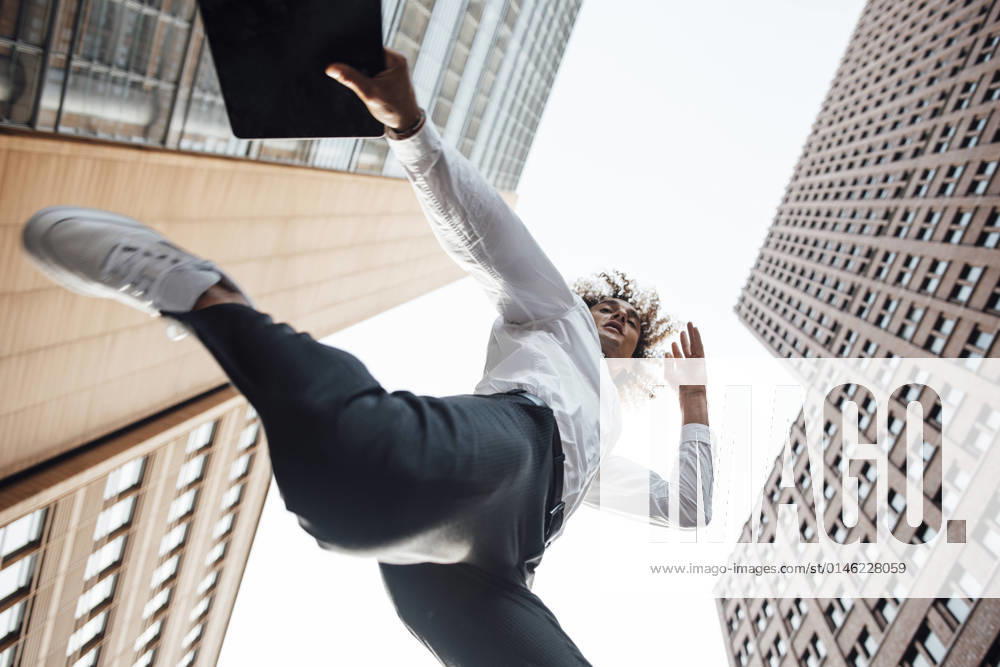 Excited businessman holding digital tablet jumping amidst office buildings model released, GUSF06710