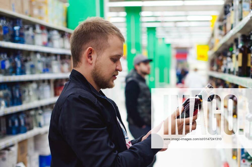 IMAGO Creative: Business, Inflation und Lieferketten bearded man, In a black jacket, stopped to make my choice in store window, holds a bottle of strong alcohol in his hand, taking from shelf model released, Symbolfoto, 26.09.2021,