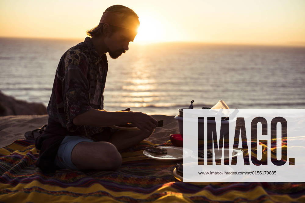 IMAGO Creative: Ende des Sommers Sunset glow over ocean as man makes picnic dinner in sand Portugal Melides, Setubal, Portugal CR_PIDODS220414-672631-01 ,model released, Symbolfoto