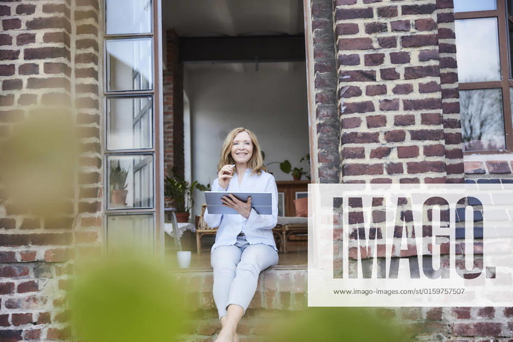IMAGO Creative: Business, Innovative Technologie-Lösungen Smiling businesswoman with tablet PC sitting on doorway model released, Symbolfoto property released, FMKF07605