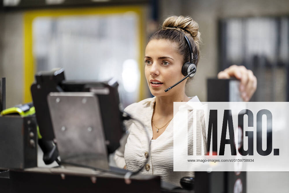 IMAGO Creative: Business, Inflation und Lieferketten Young businesswoman wearing headset operating machine in factory model released, Symbolfoto property released, PESF03754